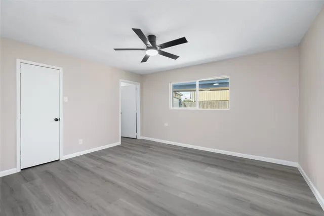 a view of an empty room with wooden floor and a ceiling fan