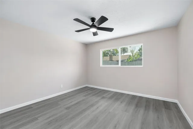an empty room with wooden floor ceiling fan and windows
