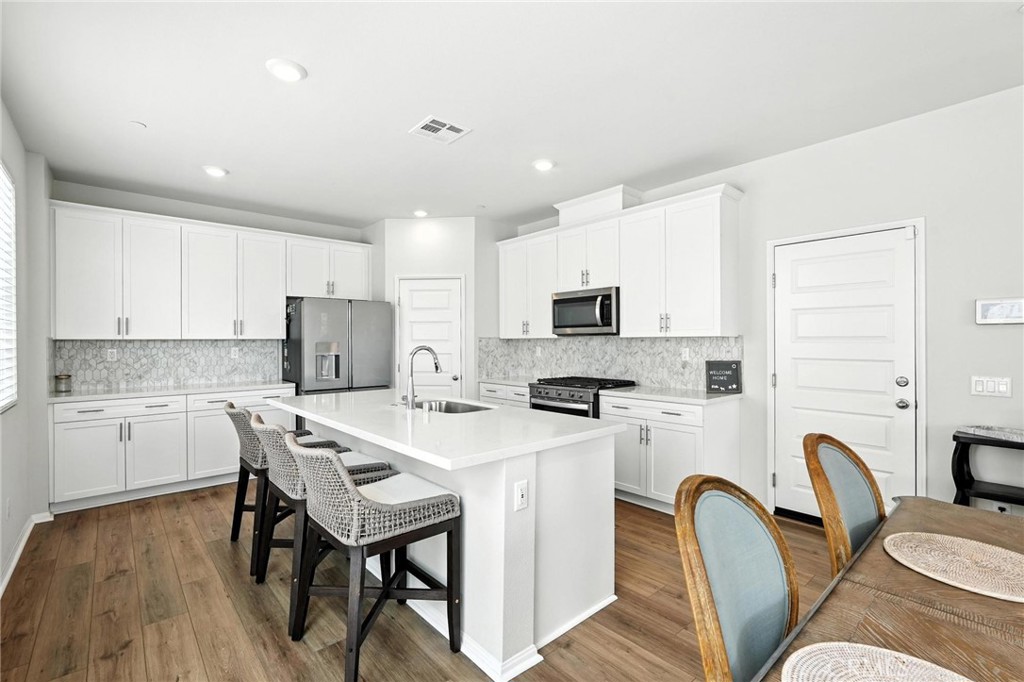 28267 Ashtree Street Temecula, CA 92591 - Photo 7 of 41 a kitchen with stainless steel appliances a white refrigerator a stove top oven a sink dishwasher a dining table and chairs with wooden floor