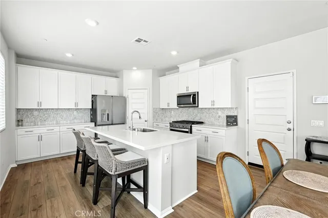 a kitchen with stainless steel appliances a microwave a sink a stove a refrigerator cabinets a dining table and chairs