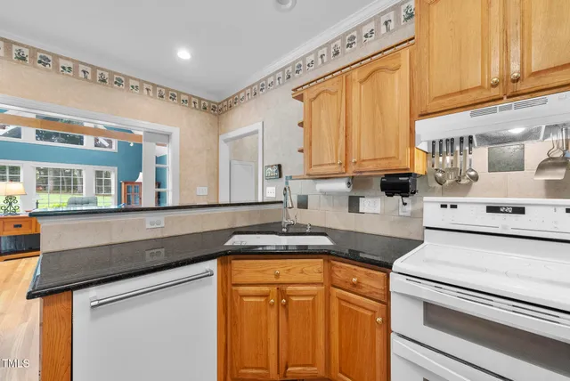 a kitchen with stainless steel appliances a stove a sink a refrigerator white cabinets and couches with wooden floor