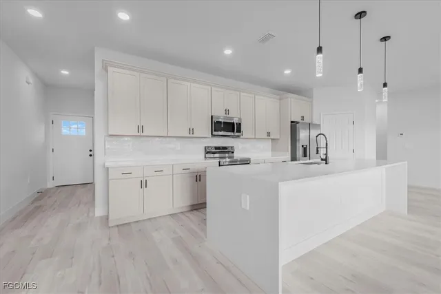 a kitchen with stainless steel appliances granite countertop a sink a stove a refrigerator and white cabinets with wooden floor