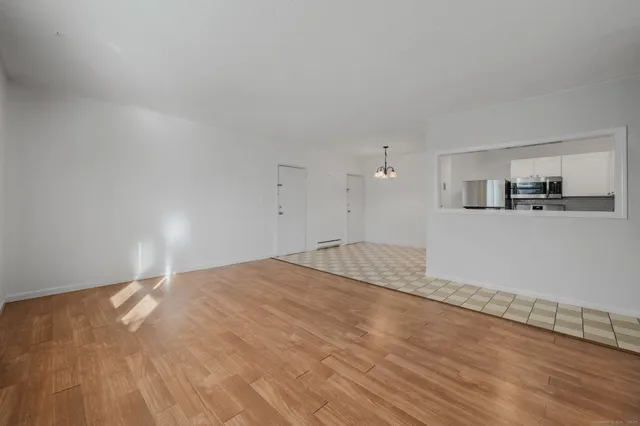 a view of empty room with wooden floor and kitchen