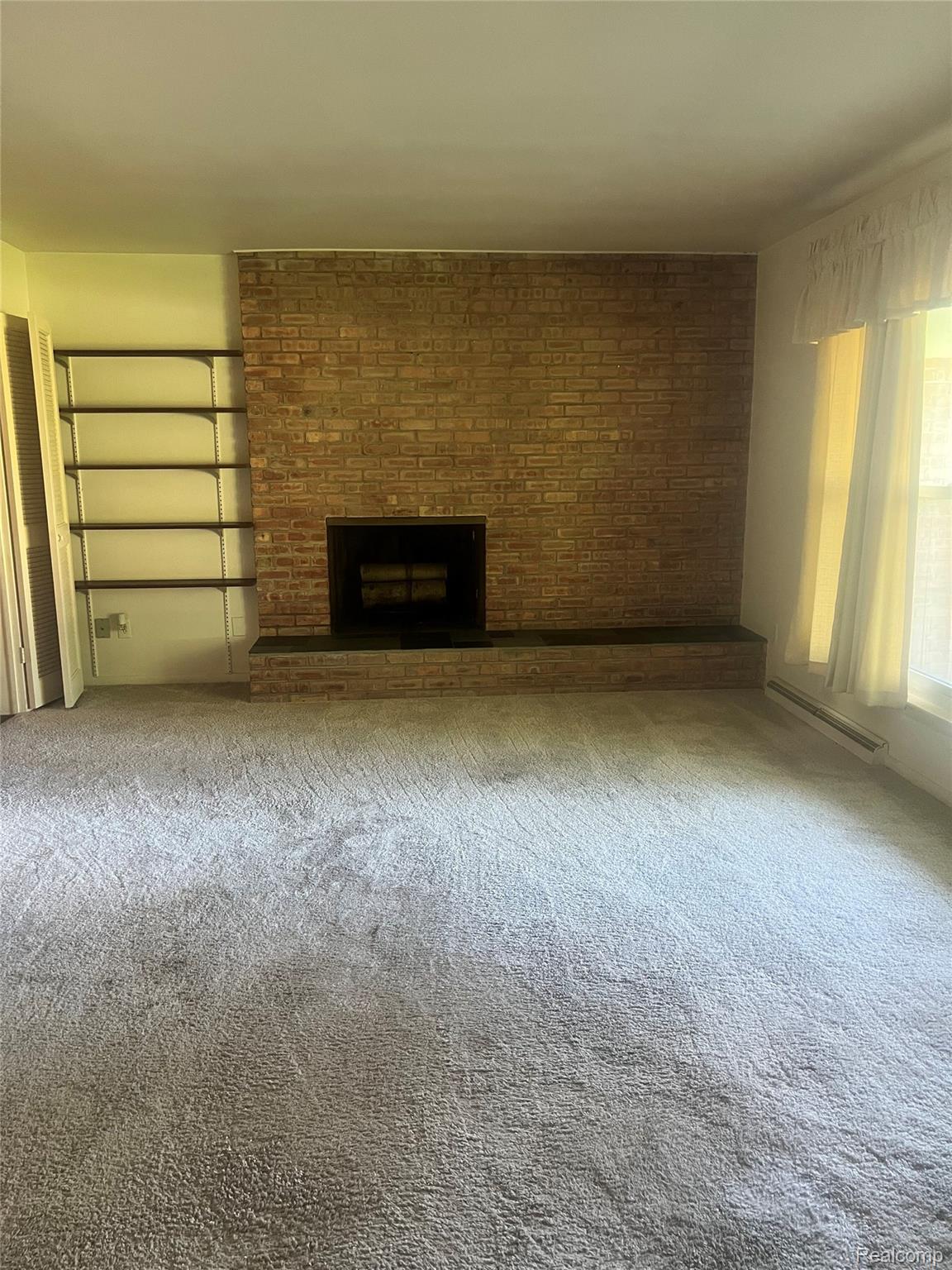 3063 West Britton Road Perry, MI 48872 - Photo 13 of 32 Brick fireplace with hearth, built-in shelving, carpeted flooring, and a large window