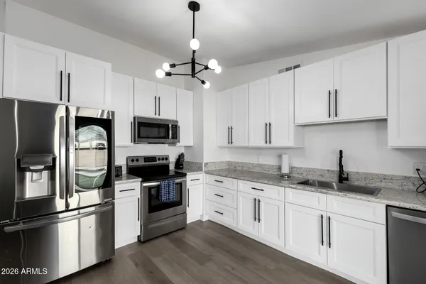 a kitchen with stainless steel appliances granite countertop a refrigerator a stove a sink and white cabinets