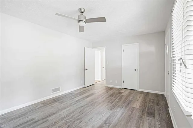 an empty room with wooden floor ceiling fan and windows