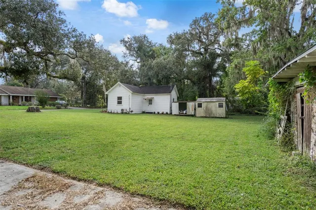 a view of a white house in front of a big yard with large trees