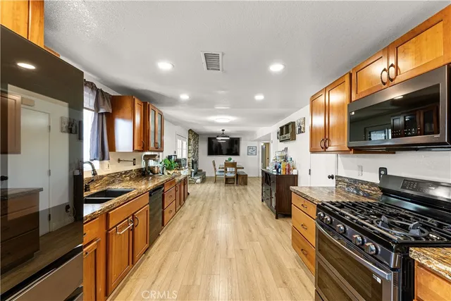 a kitchen with stainless steel appliances a stove top oven a sink dishwasher a refrigerator and white cabinets with wooden floor