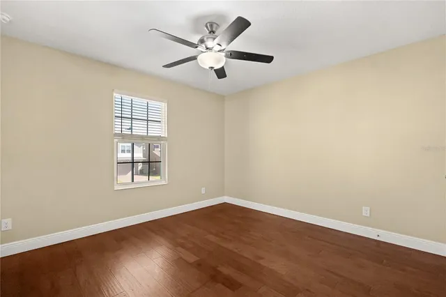 an empty room with wooden floor chandelier fan and windows