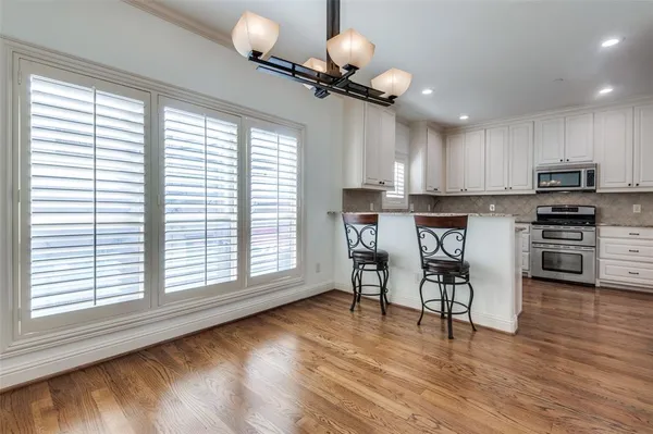 a kitchen with stainless steel appliances granite countertop a stove top oven a refrigerator a dining table and chairs with wooden floor