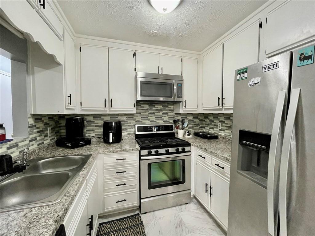 766 Country Club Road Newnan, GA 30263 - Photo 16 of 34 Kitchen featuring appliances with stainless steel finishes, decorative backsplash, light marble finish floors, white cabinetry, and a textured ceiling