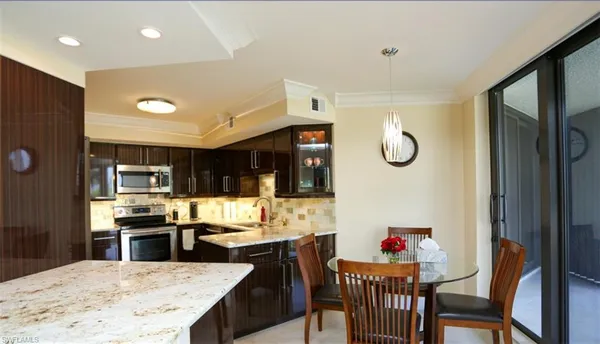 a kitchen with stainless steel appliances kitchen island granite countertop a refrigerator a stove top oven and a dining table with wooden floor
