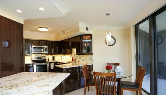 a kitchen with stainless steel appliances kitchen island granite countertop a refrigerator a stove top oven and a dining table with wooden floor