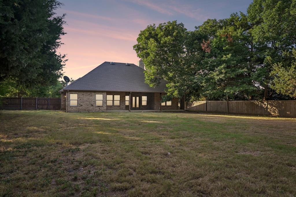 2617 Kirby Road Rowlett, TX 75088 - Photo 31 of 35 Expansive lawn with mature trees and a privacy fence, showcasing a brick exterior with multiple windows and a covered patio