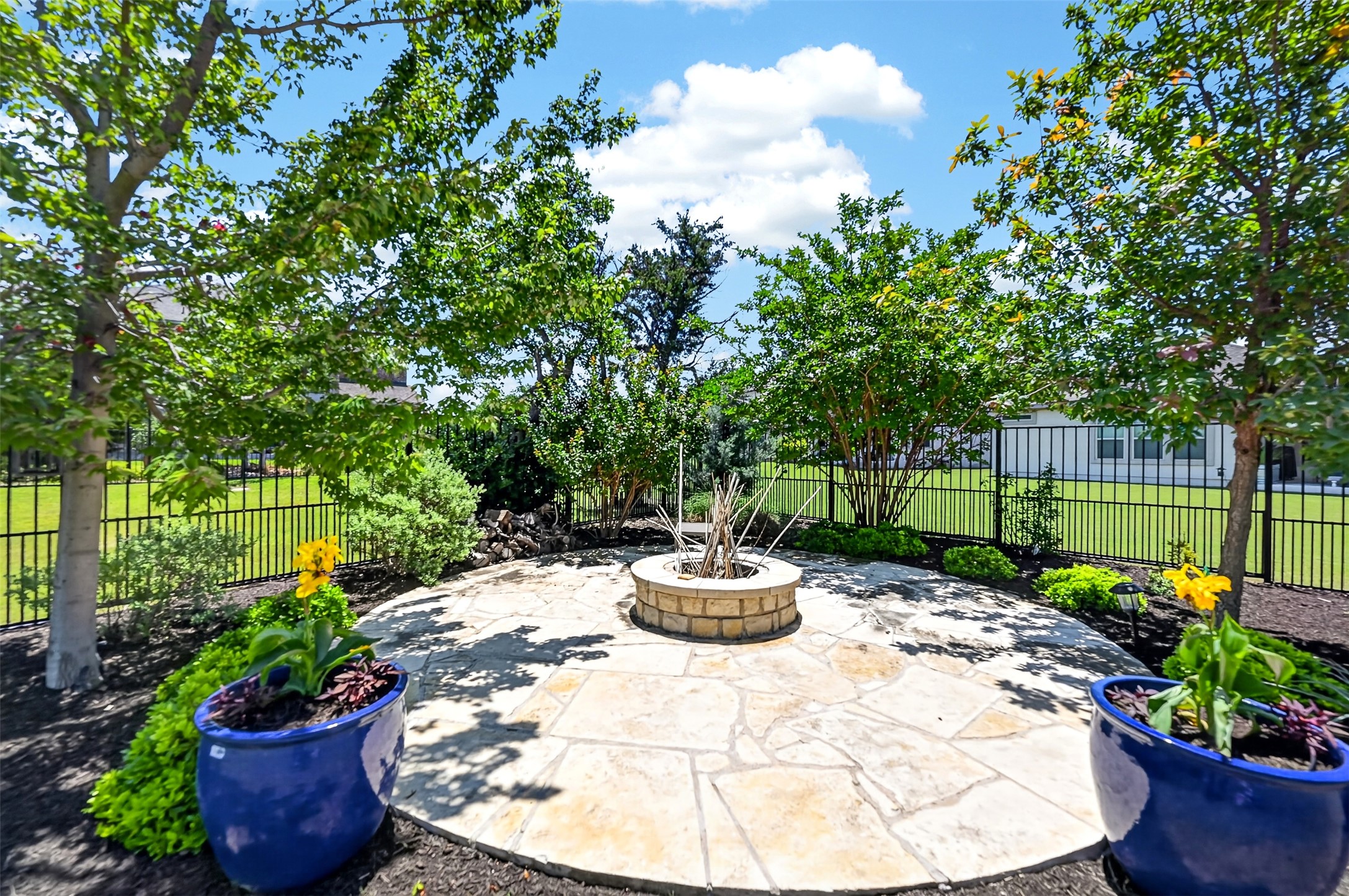 1201 Positano Pass Leander, TX 78641 - Photo 31 of 40 Backyard patio featuring irregular flagstone, a built-in stone fire pit, mature trees, and a black wrought iron fence