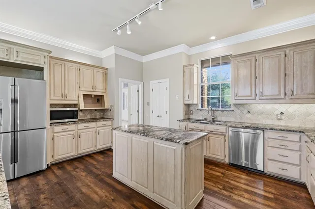 a kitchen with stainless steel appliances granite countertop a stove a sink dishwasher a refrigerator and white cabinets with wooden floor