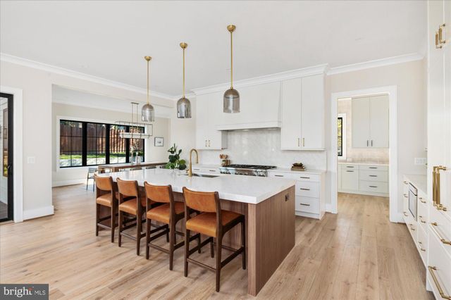 a large kitchen with stainless steel appliances sink a stove and white cabinets with wooden floor