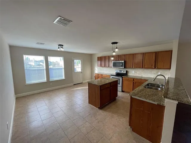 a kitchen with stainless steel appliances granite countertop a stove top oven a sink a dining table and chairs