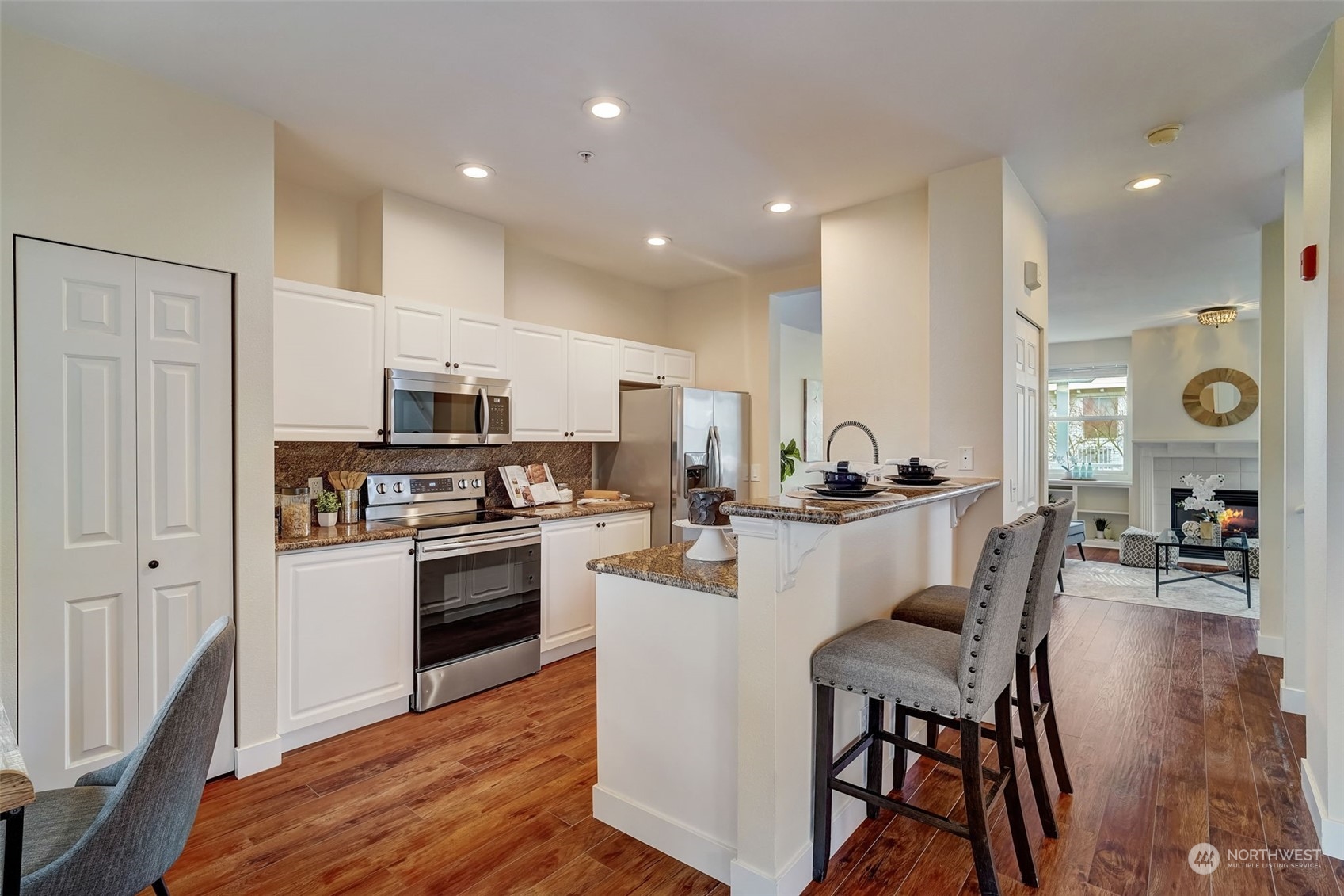 11873 Northeast 162nd Lane, Unit 121 Bothell, WA 98011 - Photo 5 of 32 a kitchen with stainless steel appliances kitchen island granite countertop a stove top oven a sink a refrigerator with white cabinets and wooden floor