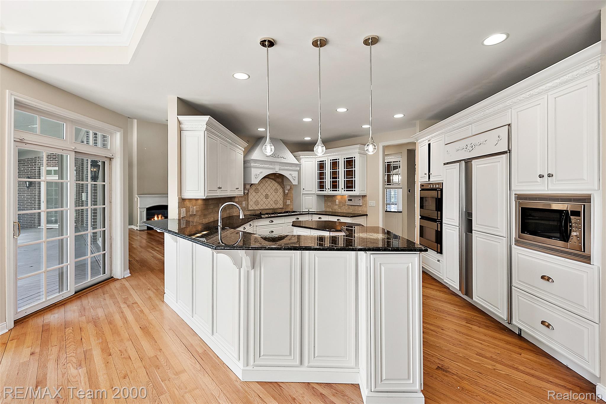 630 Sheldon Court Rochester, MI 48306 - Photo 32 of 94 Kitchen featuring dark stone counters, a peninsula, pendant lighting, white cabinetry, and a lit fireplace