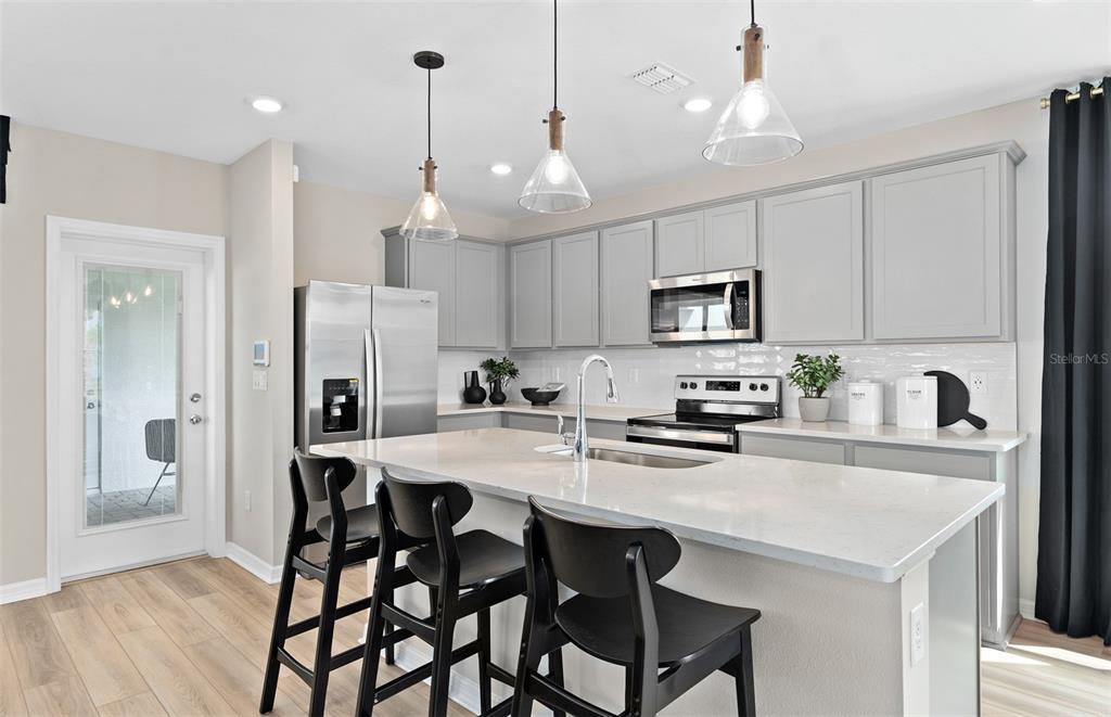 5013 Furrowed Way St. Cloud, FL 34771 - Photo 6 of 26 a kitchen with stainless steel appliances granite countertop a stove a refrigerator a sink a dining table and chairs with wooden floor