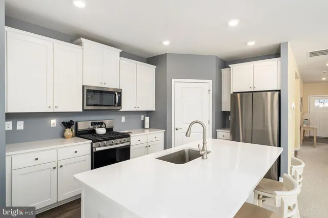 a kitchen with stainless steel appliances a sink a stove a refrigerator with white cabinets