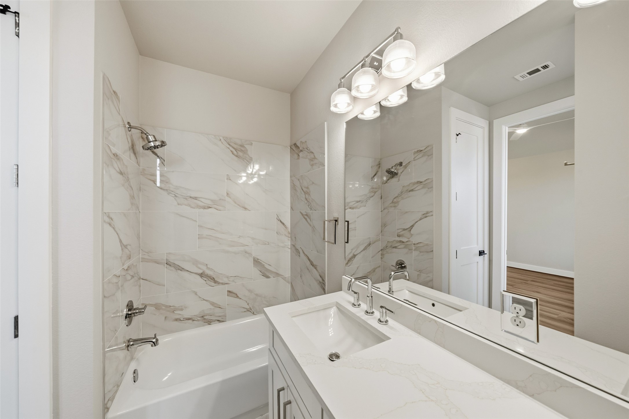 3422 Elser Street Houston, TX 77009 - Photo 14 of 26 This bathroom features a modern design with a marble-patterned tile surround for the bathtub and shower combo, a sleek vanity with a white countertop and dual sinks, and a large mirror under stylish lighting.