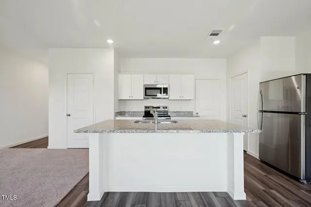 a kitchen with stainless steel appliances granite countertop a refrigerator a stove a sink and white cabinets with wooden floor