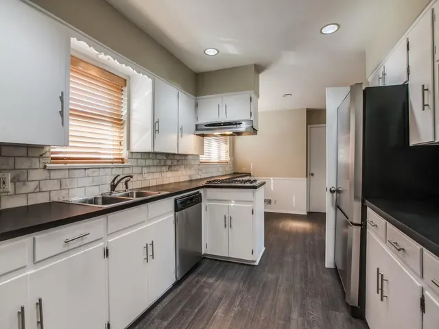 a kitchen with stainless steel appliances white cabinets a sink a window and wooden floors