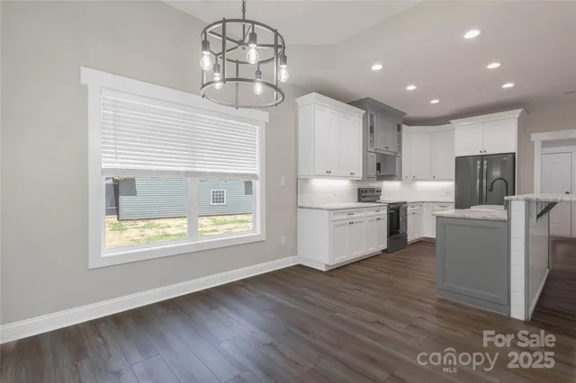 a kitchen with stainless steel appliances granite countertop a refrigerator a sink dishwasher a stove and a dining table with wooden floor