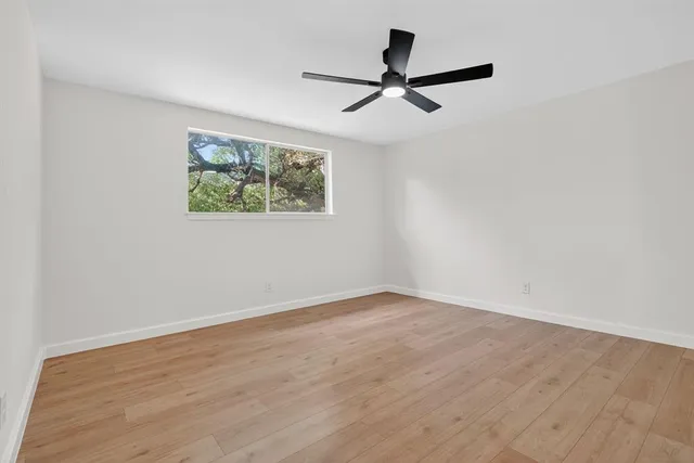 a view of a big room with wooden floor a ceiling fan and windows