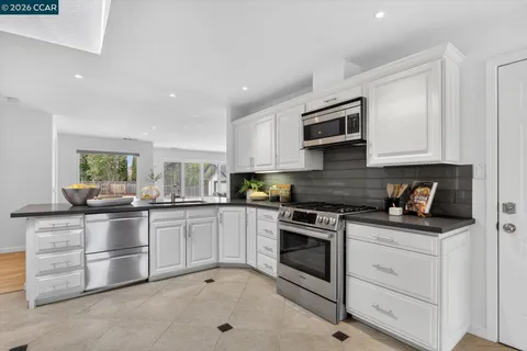 a kitchen with stainless steel appliances granite countertop white cabinets a sink a stove a microwave and a refrigerator