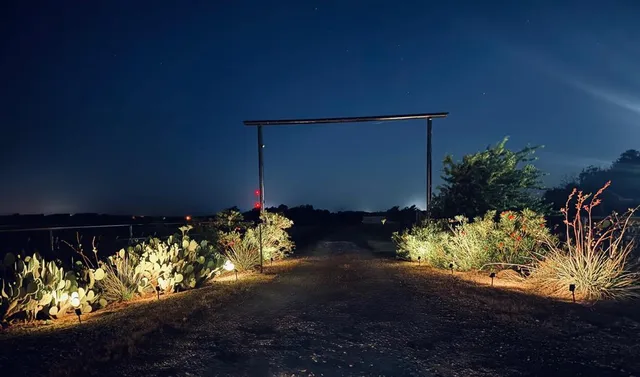 a view of a fountain with some plants in front of yellow house