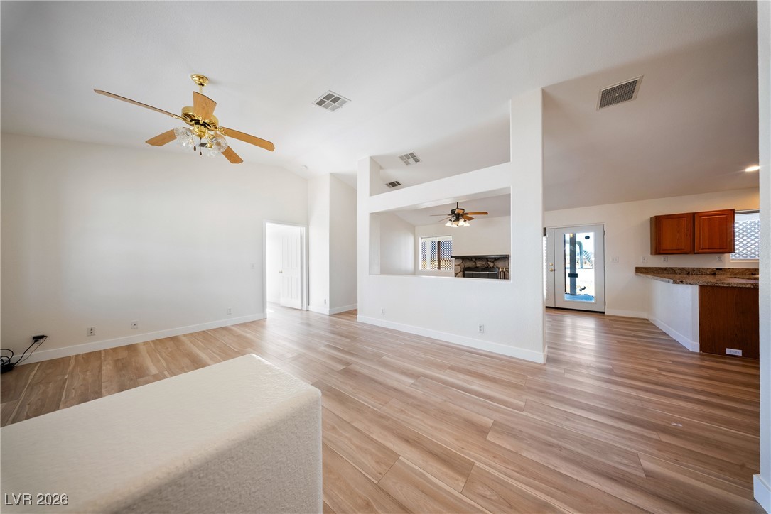 2420 Tough Boy Road Pahrump, NV 89060 - Photo 3 of 54 Unfurnished living room with ceiling fan, vaulted ceiling, a stone fireplace, and light wood-type flooring