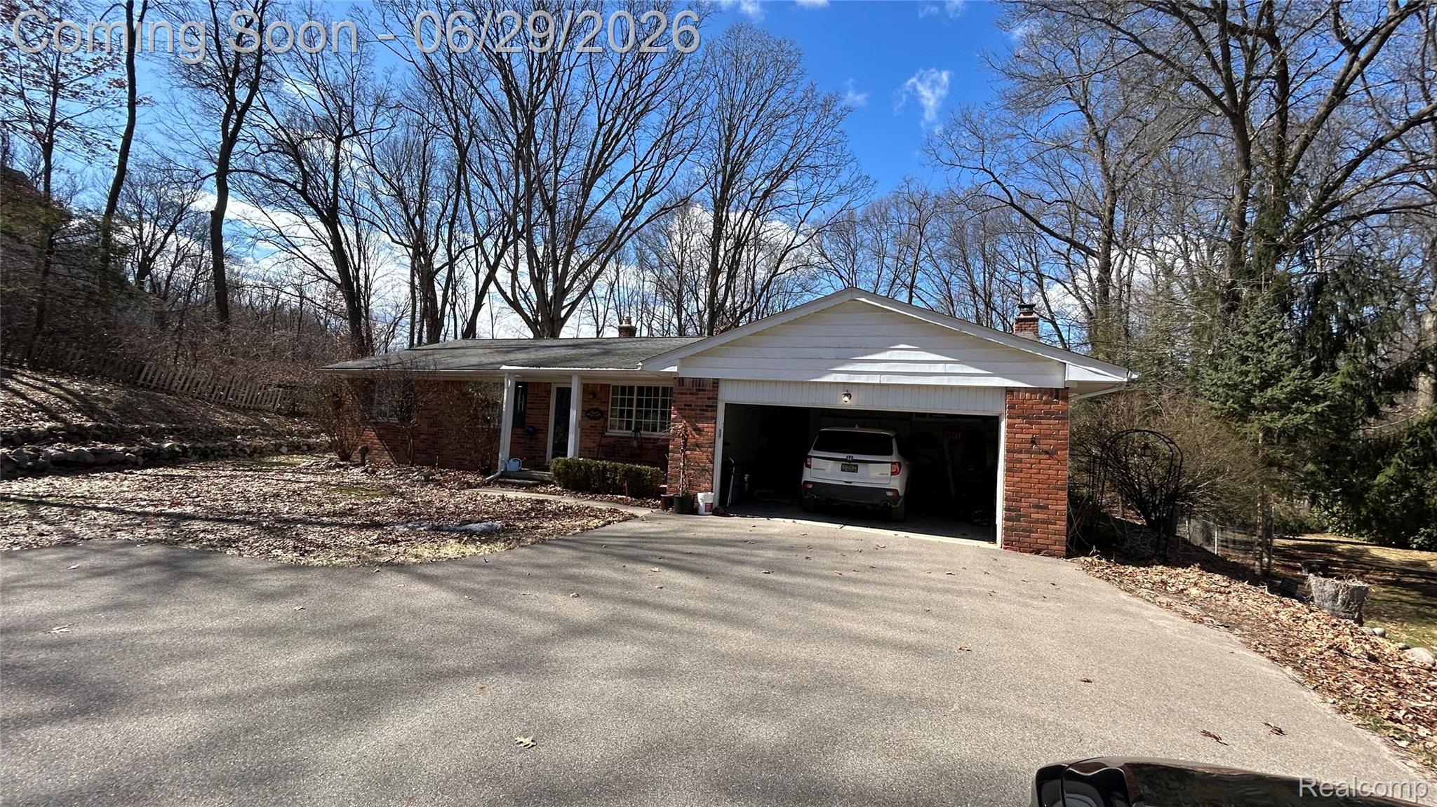 Brick ranch home featuring a two-car attached garage, paved driveway, and covered front entry