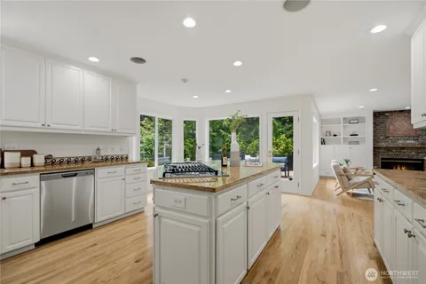 a kitchen with stainless steel appliances granite countertop a stove a sink dishwasher a refrigerator and white cabinets with wooden floor