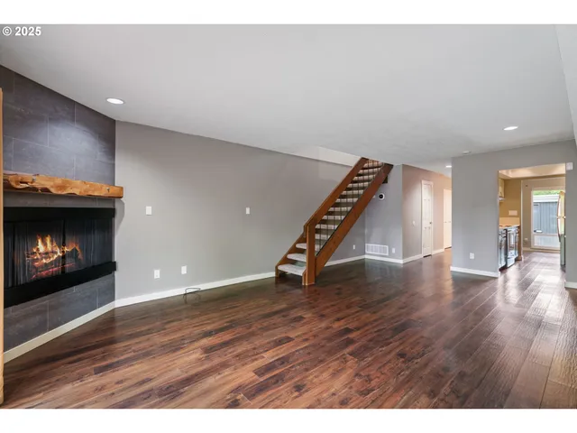 a view of an empty room with wooden floor fire place and staircase