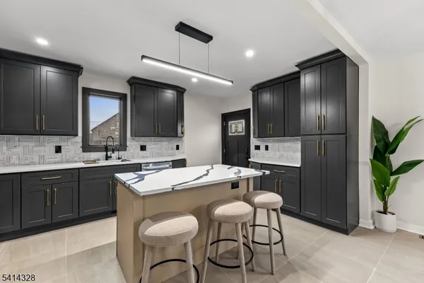 a kitchen with stainless steel appliances a sink a stove a refrigerator and chairs