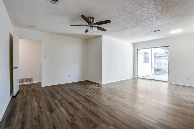 a view of an empty room with wooden floor and a ceiling fan
