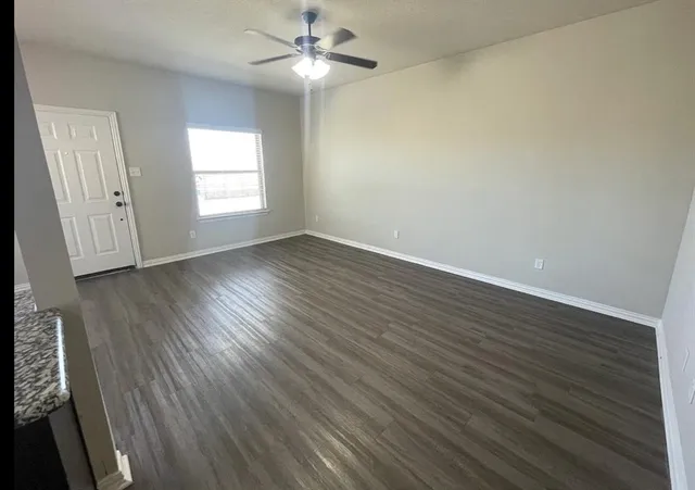 an empty room with wooden floor fan and windows