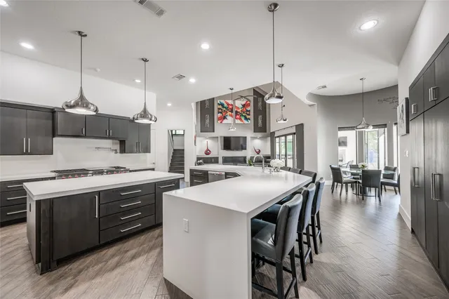 a kitchen with stainless steel appliances kitchen island granite countertop a dining table chairs sink and white cabinets