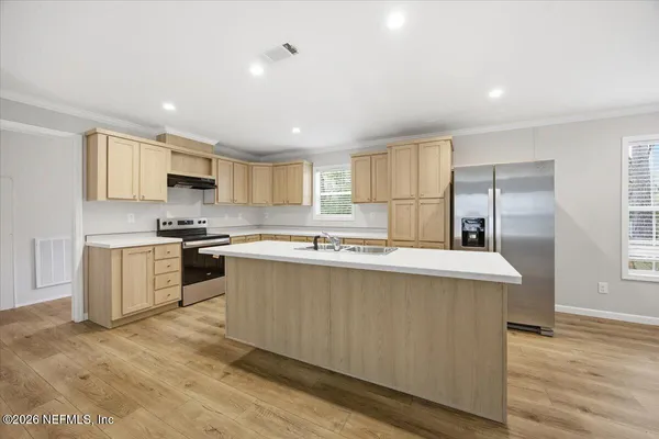 a kitchen with stainless steel appliances a sink a stove a refrigerator cabinets and a window