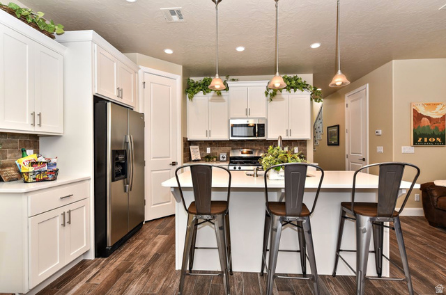 1622 Canyon Tree Drive St. George, UT 84770 - Photo 3 of 34 Kitchen featuring white cabinetry, stainless steel appliances, wood-finish flooring, a central island with bar seating, and pendant lighting