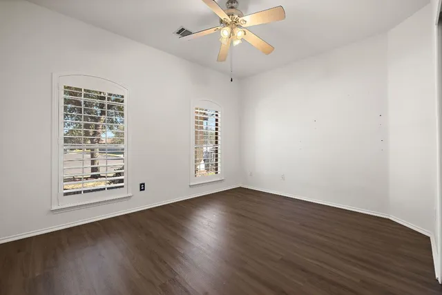 an empty room with wooden floor chandelier fan and windows