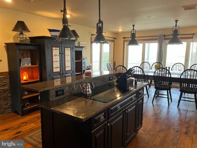 a kitchen with stainless steel appliances granite countertop a refrigerator a sink dishwasher a stove and a dining table with wooden floor