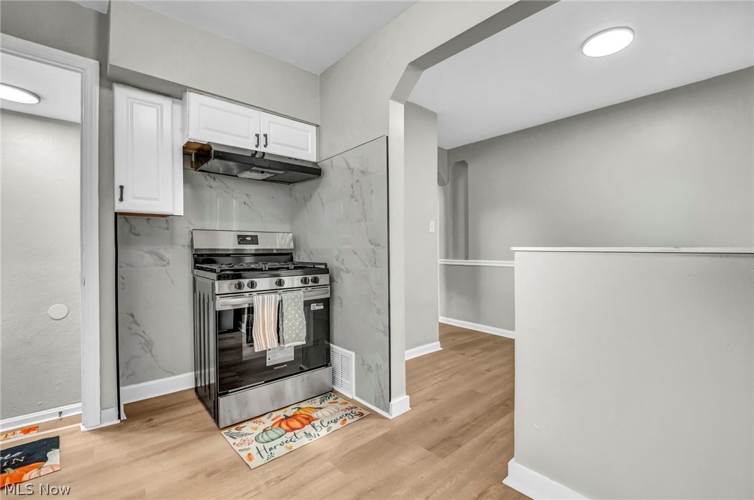 4250 Verona Road South Euclid, OH 44121 - Photo 11 of 31 Stainless steel range with coordinating range hood, white upper cabinetry, and a marbled-finish backsplash