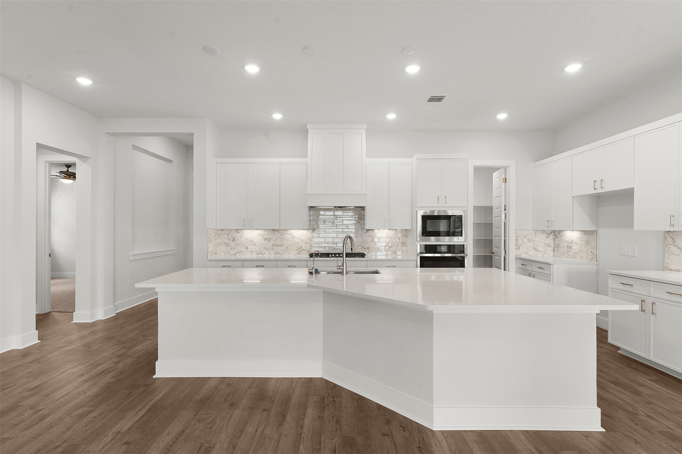 1129 Pansy Trail Georgetown, TX 78628 - Photo 12 of 29 Expansive kitchen featuring a large white island with a sink, white cabinetry, integrated stainless steel appliances, and wood-finish flooring