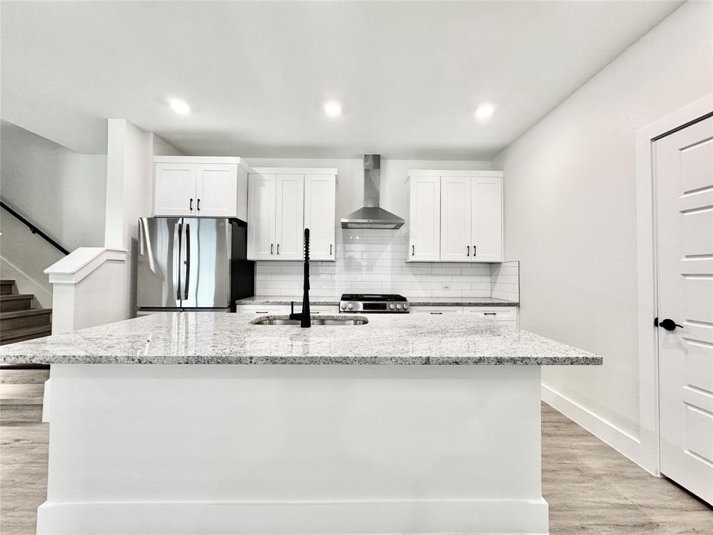 8509 Shorehan Road The Colony, TX 75056 - Photo 4 of 33 Kitchen featuring stainless steel appliances, wall chimney exhaust hood, a sink, white cabinetry, and a kitchen island with sink