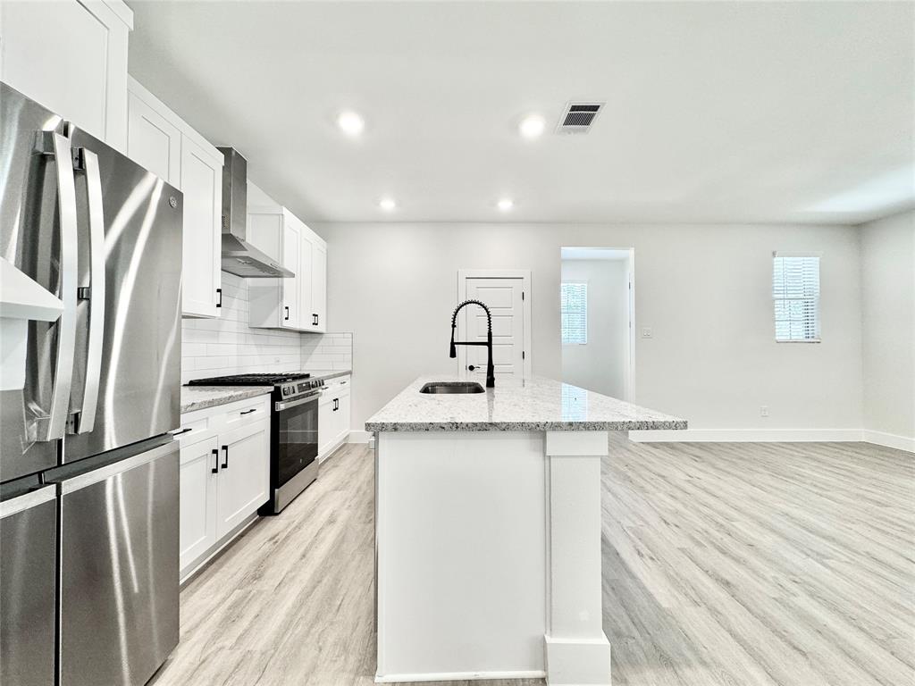 8509 Shorehan Road The Colony, TX 75056 - Photo 6 of 33 Kitchen with appliances with stainless steel finishes, a sink, wall chimney range hood, light wood-style flooring, and an island with sink