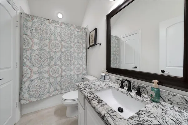 a bathroom with a granite countertop sink toilet a mirror and shower curtain